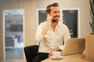 Man holding cellphone in front of laptop computer.